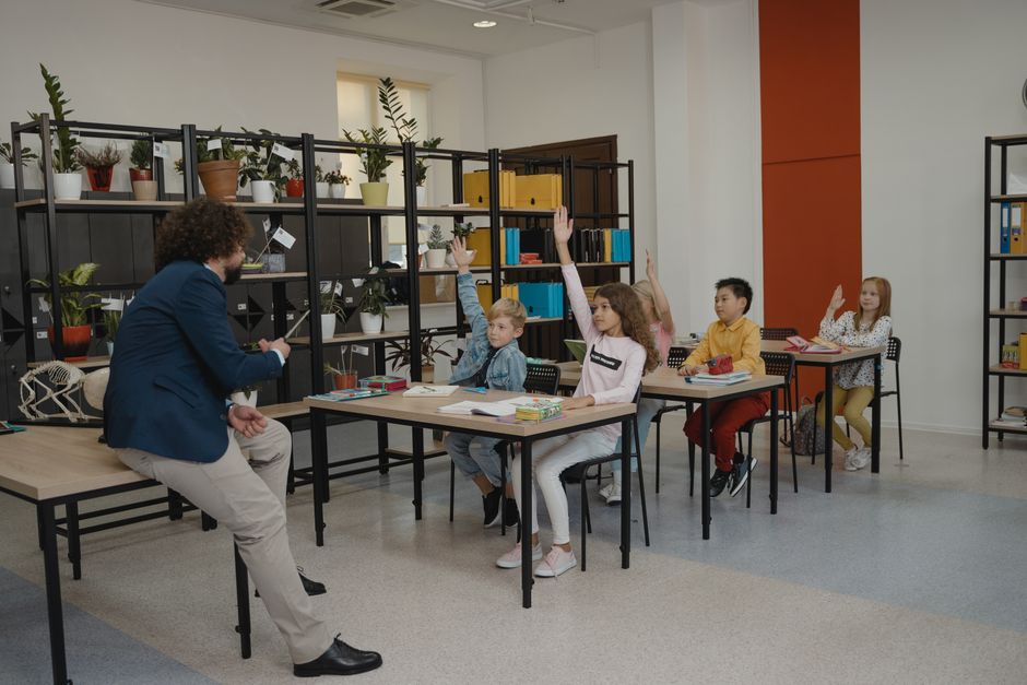 Učenici aktivno dižu ruke u modernoj učionici uz pažljivu nastavnicu.